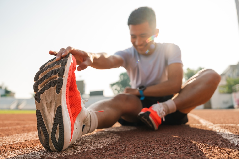 Man stretching leg muscles after workout on running track smiling enjoying fitness routine